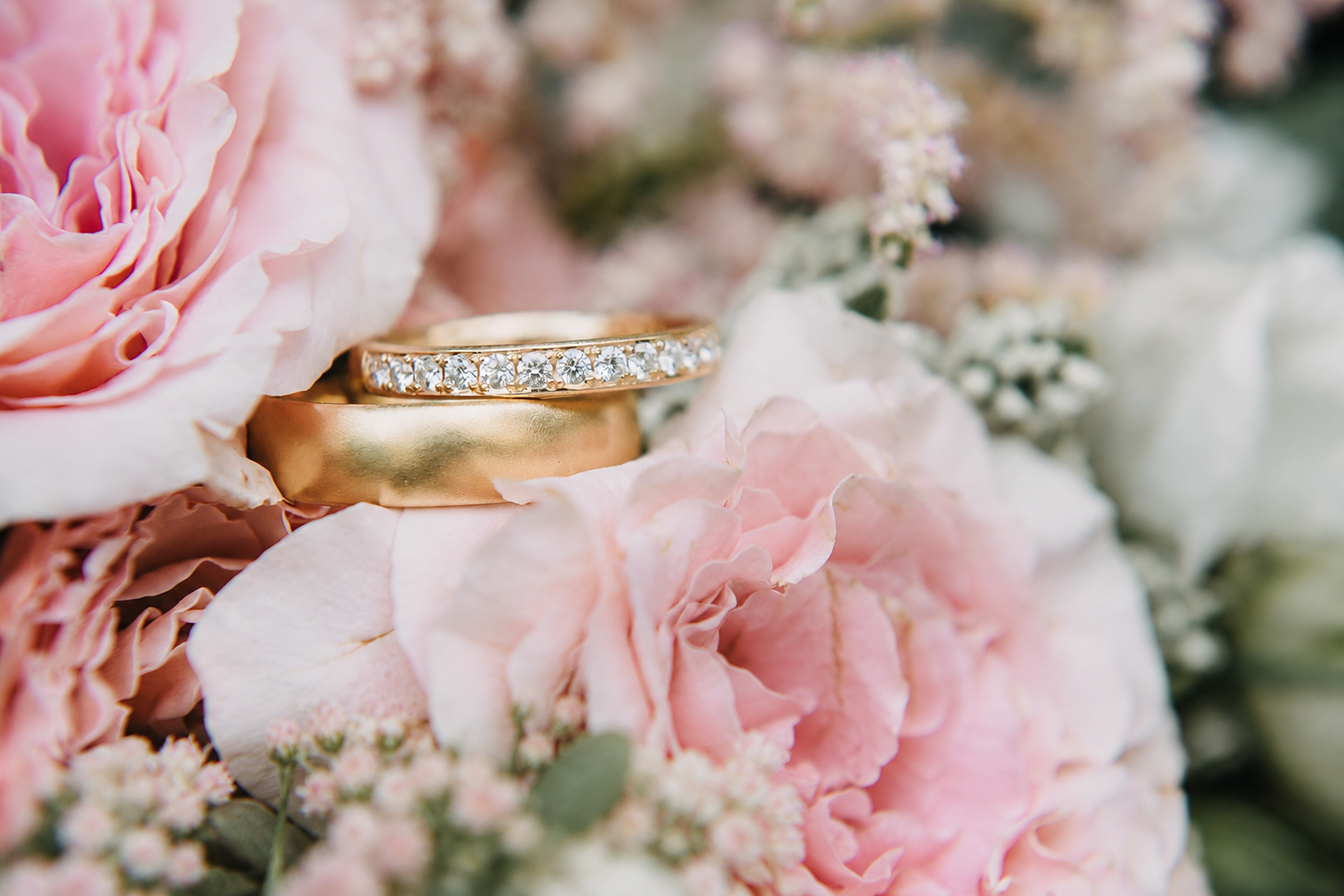 Handgefertigte Trauringe aus Gelbgold zwischen rosafarbenen Blumen