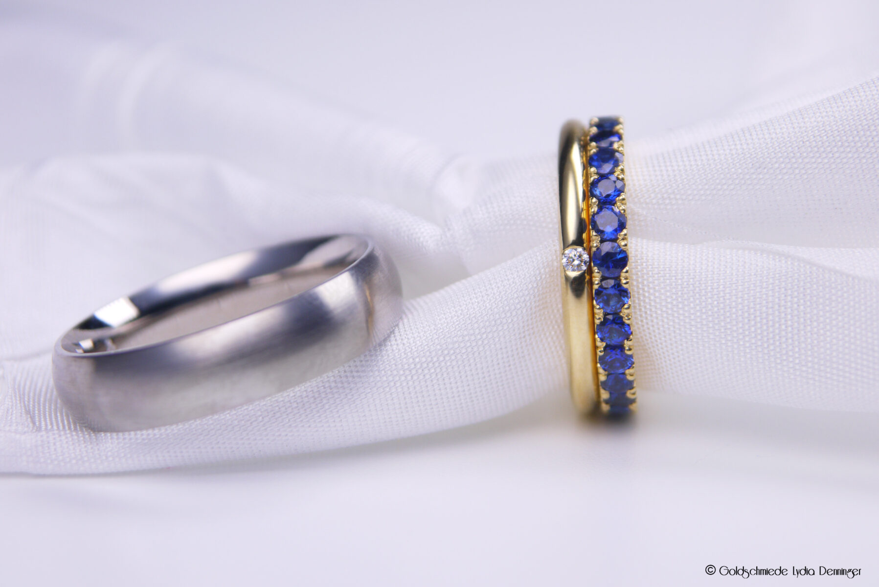 Der Herren-Ehering besteht aus 500 Palladium, der Damen-Ehering aus 750/18k Gelbgold mit einem eingeriebenen Brillanten. Dazu wurde ein Memoire-Saphir-Zusteckring in 750/18k Gelbgold mit Saphiren unter dem Mikroskop gefasst.