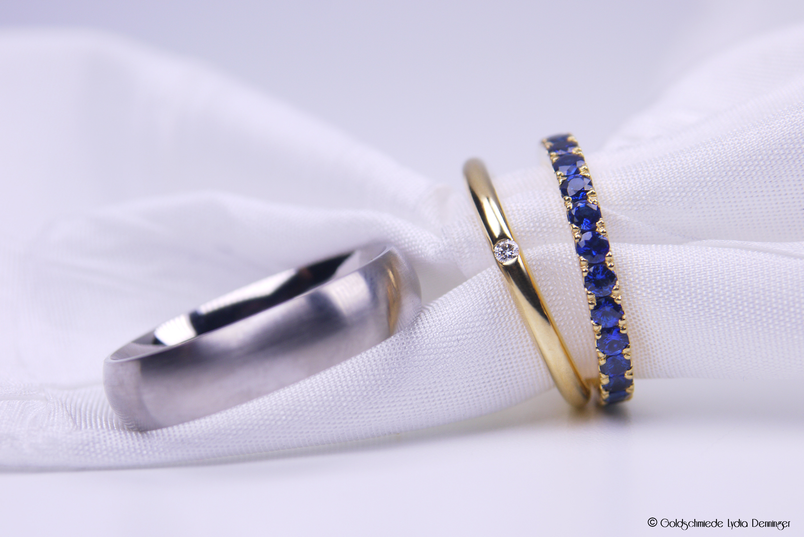Der Herren-Ehering besteht aus 500 Palladium, der Damen-Ehering aus 750/18k Gelbgold mit einem eingeriebenen Brillanten. Dazu wurde ein Memoire-Saphir-Zusteckring in 750/18k Gelbgold mit Saphiren unter dem Mikroskop gefasst.
